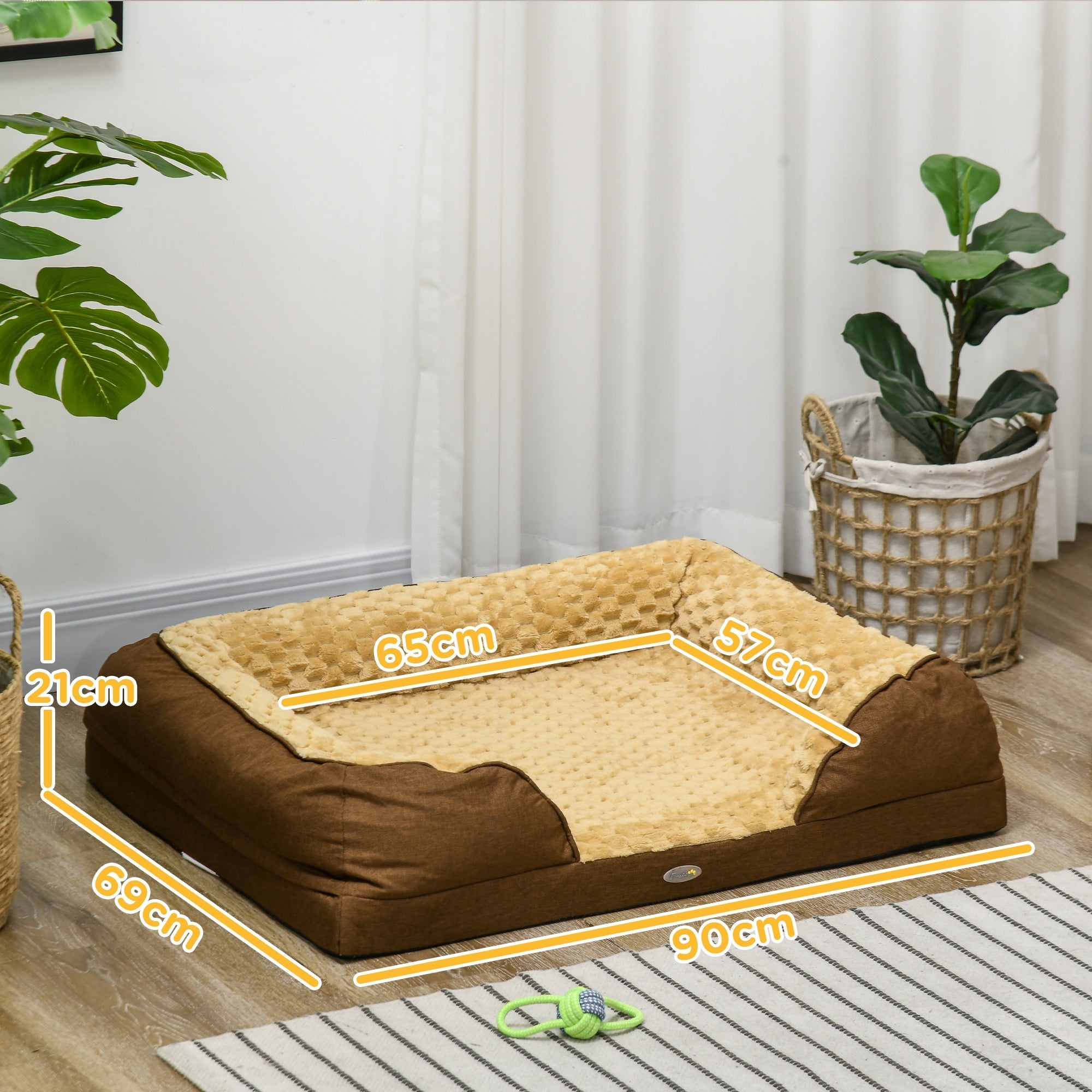 Brown pet bed with measurements in a room with plants and a curtain.