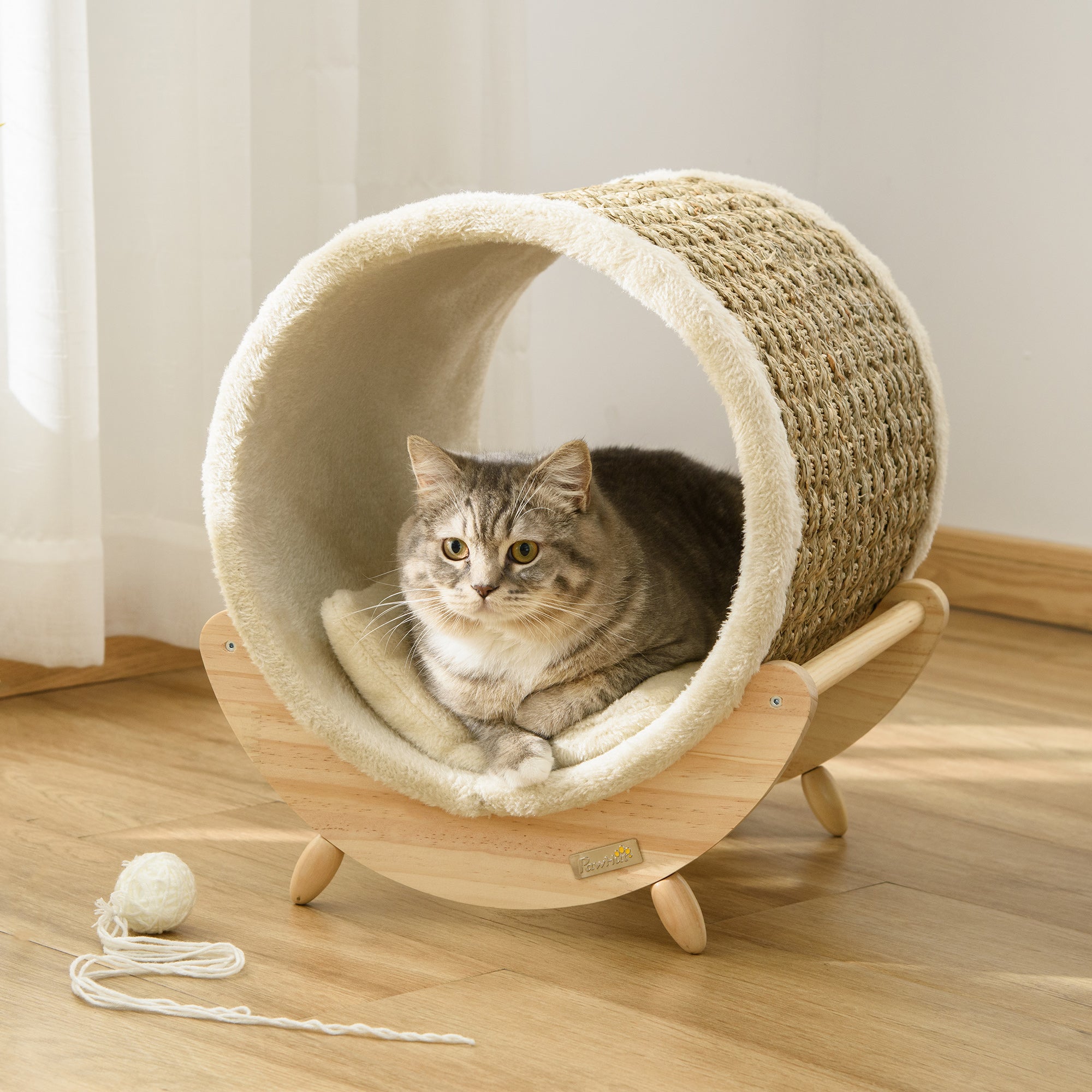 Cat lying inside a cylindrical pet bed with wooden base on a wooden floor.