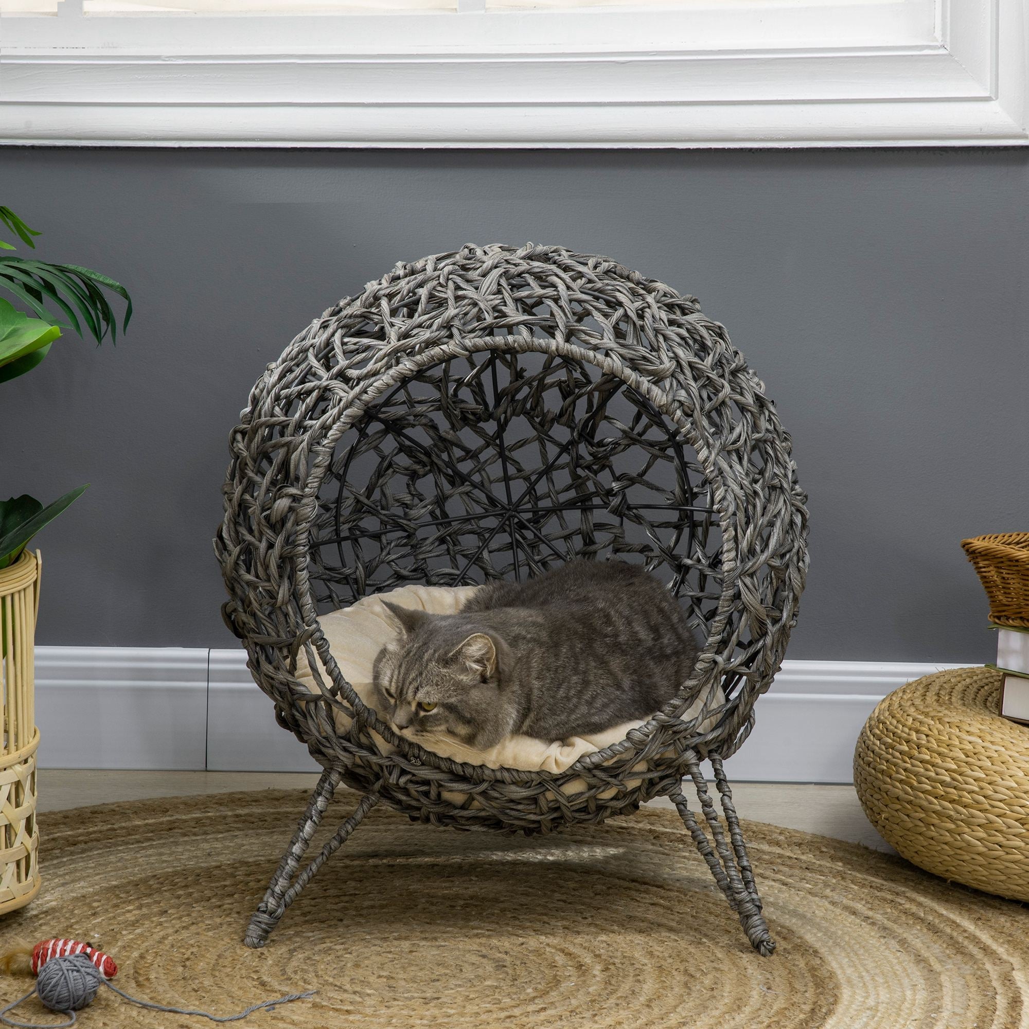 Woven pet bed with a cat inside, placed on a textured rug against a gray wall.