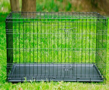Black metal pet crate on grass with trees in the background
