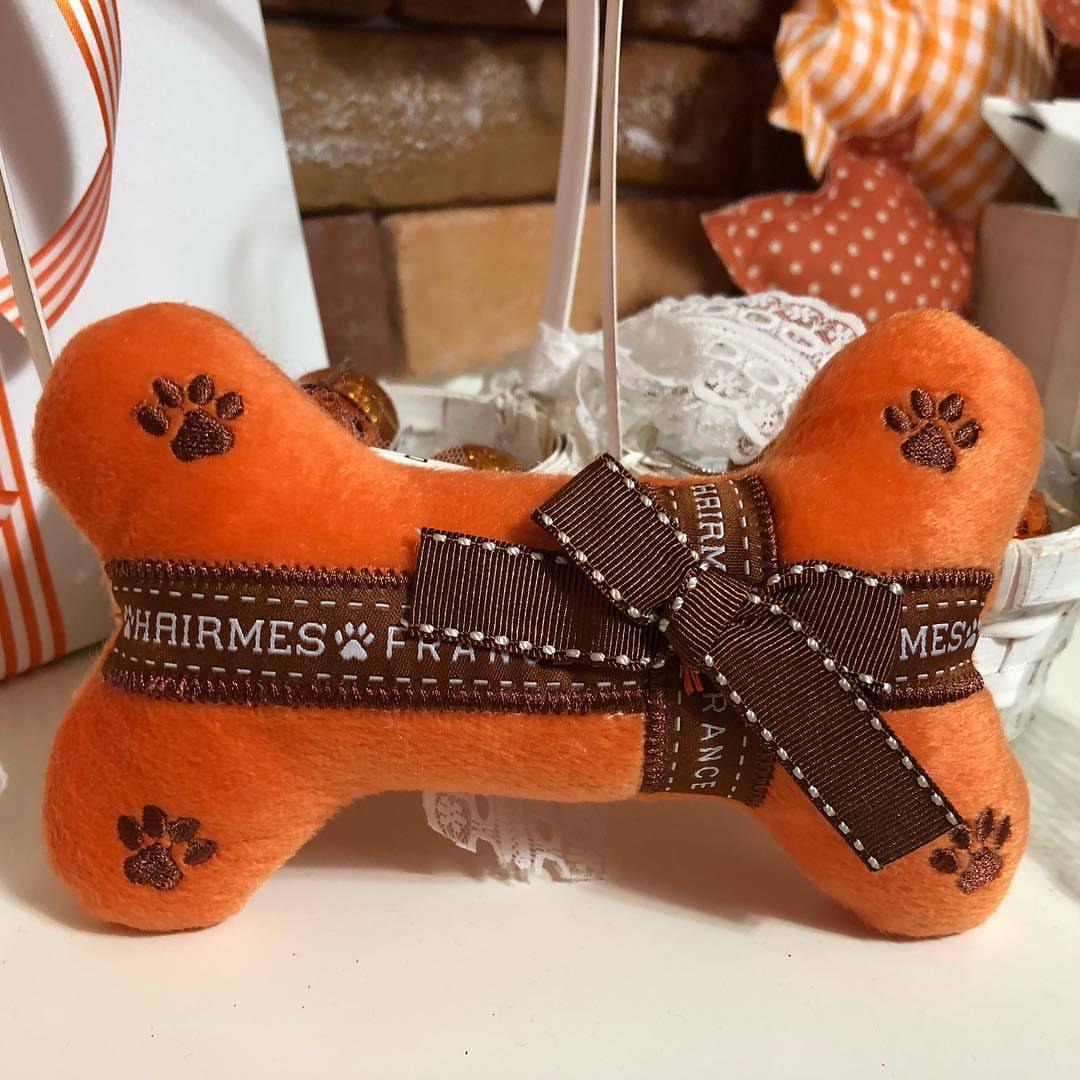 Orange bone-shaped toy with a brown ribbon and 'Whimzees' branding on a blurred background.